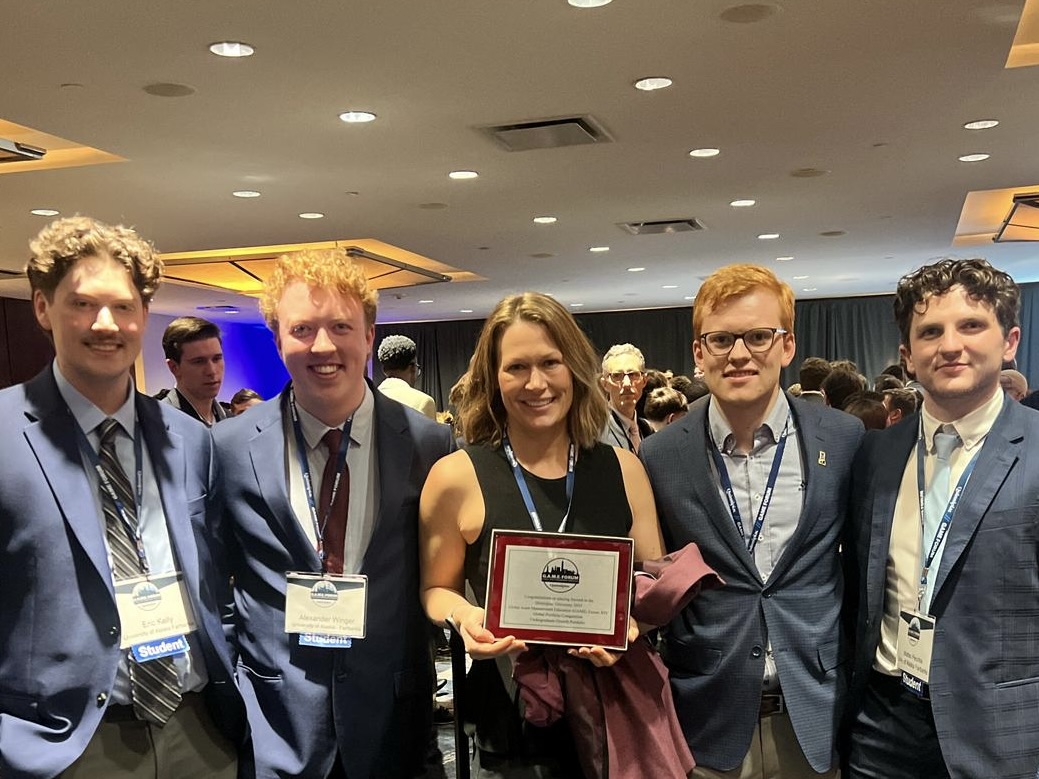 four college students stand with professor, holding a certificate at professional conference