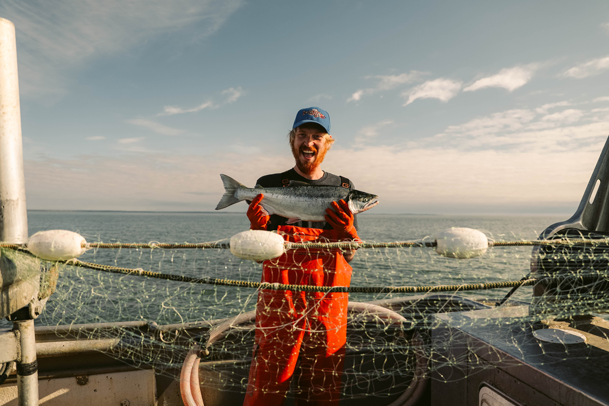 Nels Ure on a fishing boat holding a salmon. Photo courtesy of Ure