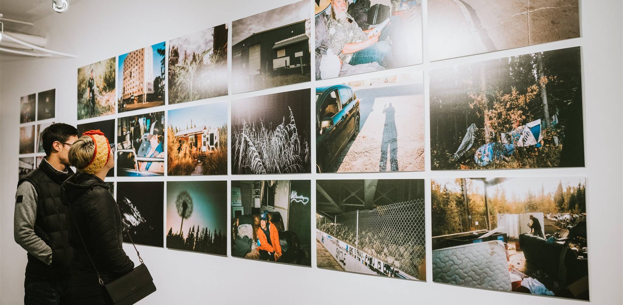 Two visitors examine a grid of photos from Sarah Manriquez's Finding Home exhibition