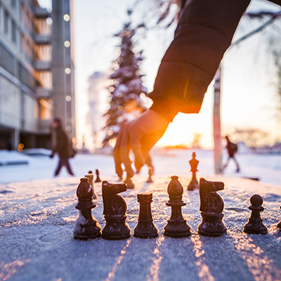 A hand reaches down contemplating its next move over an outdoors chess board