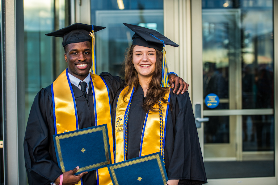 Honors students in their graduation regalia holding deploma covers