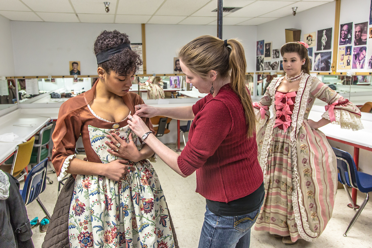 Technical Theatre Facilities Assistant professor Bethany Marx helps Nicole Cowans into her costume before Cowans, Katrina Kuharich (right) and other members of the cast of Theatre UAF's production of "Tartuffe" performed a live teaser in Wood Center a couple of days before opening night. | UAF Photo by Todd Paris, 2014